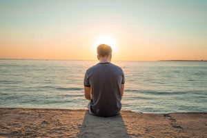 man sitting on beach at sunset - Karuna Counselling